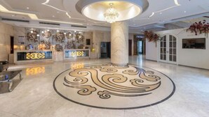 A spacious lobby with a central decorative column, a reception desk, and a chandelier.