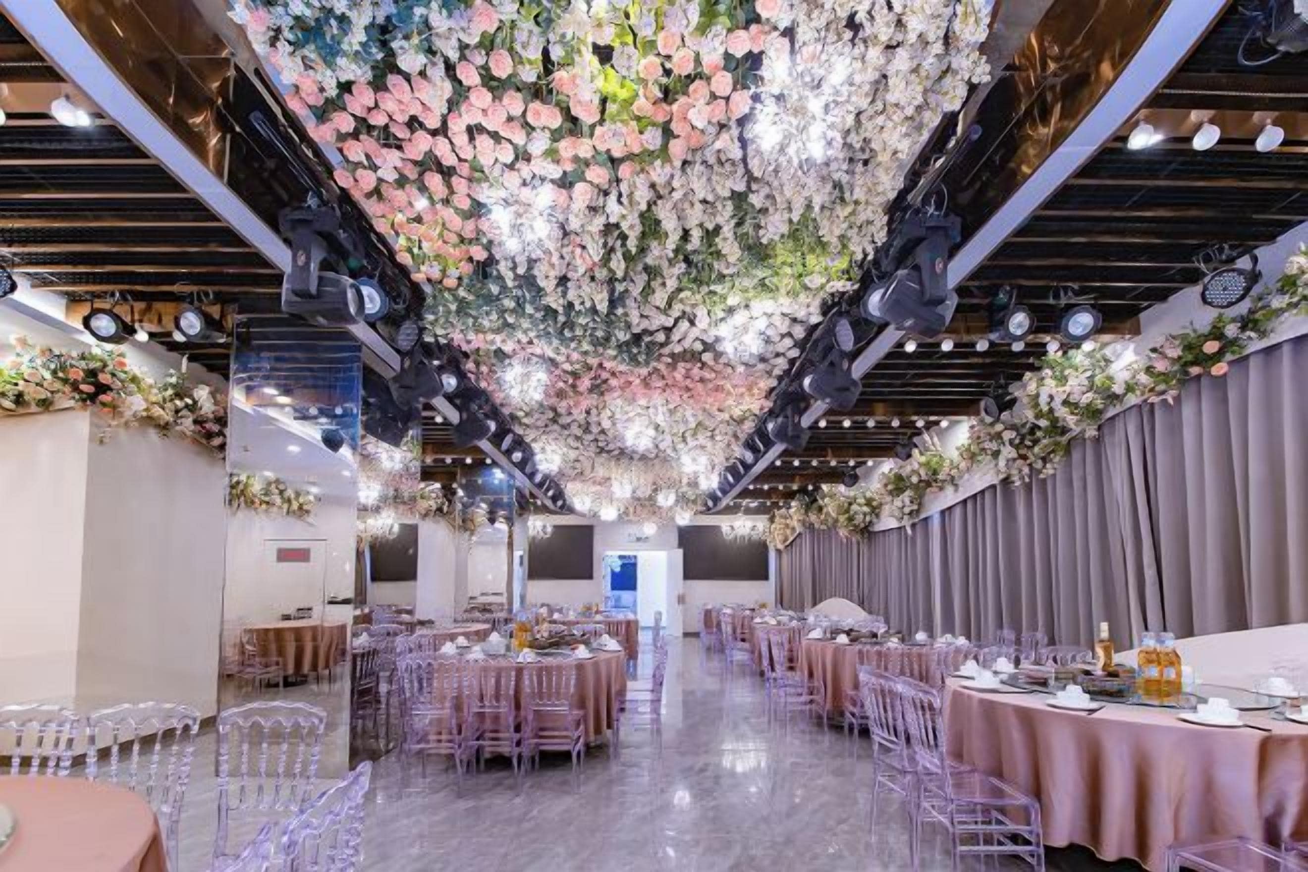A banquet hall with round tables, chairs, and a floral ceiling.
