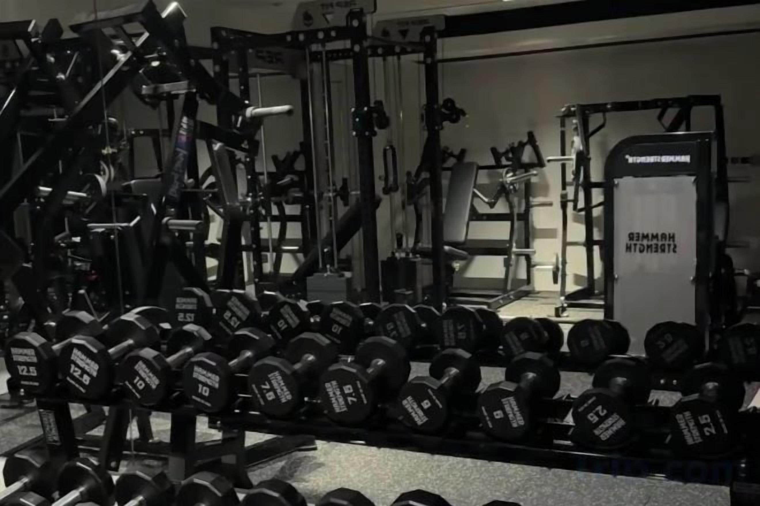 A gym with various weightlifting equipment and dumbbells.