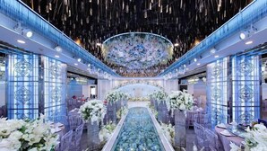 A luxurious hotel lobby with a central glass walkway, elegant floral arrangements, and a decorative ceiling.