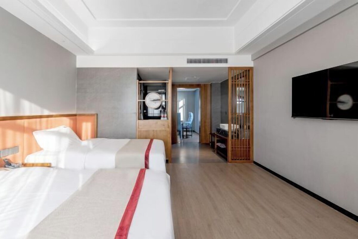 A hotel room with a large bed, a TV mounted on the wall, and a wooden wardrobe.
