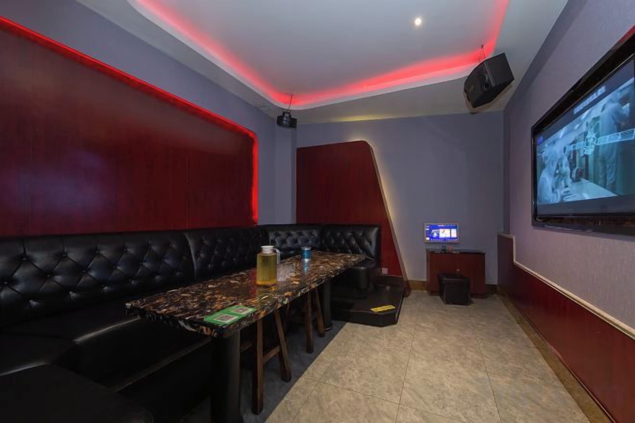 A room with a long table, black cushioned seating, a projector screen, and a television.