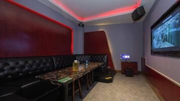 A room with a long table, black cushioned seating, a projector screen, and a television.