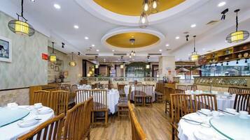 Un interior de restaurante con mesas redondas, sillas de madera y lámparas colgantes.