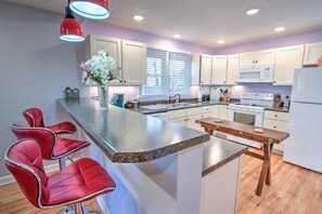 A modern kitchen with a central island, bar stools, a wooden table, and white cabinetry. - Minutes to the iconic State Street & King University. Local park in back yard! (Bristol)
