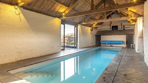 Piscina interna com teto de madeira e paredes de tijolos brancos.
