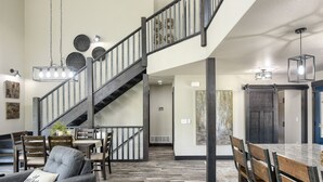 Un vaste espace de vie agrémenté d’un escalier en bois, d’une table à manger avec des chaises et d’un lustre moderne.
