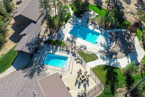 An aerial view of a residential property with two swimming pools, a patio area with outdoor furniture, and a large fenced yard.
