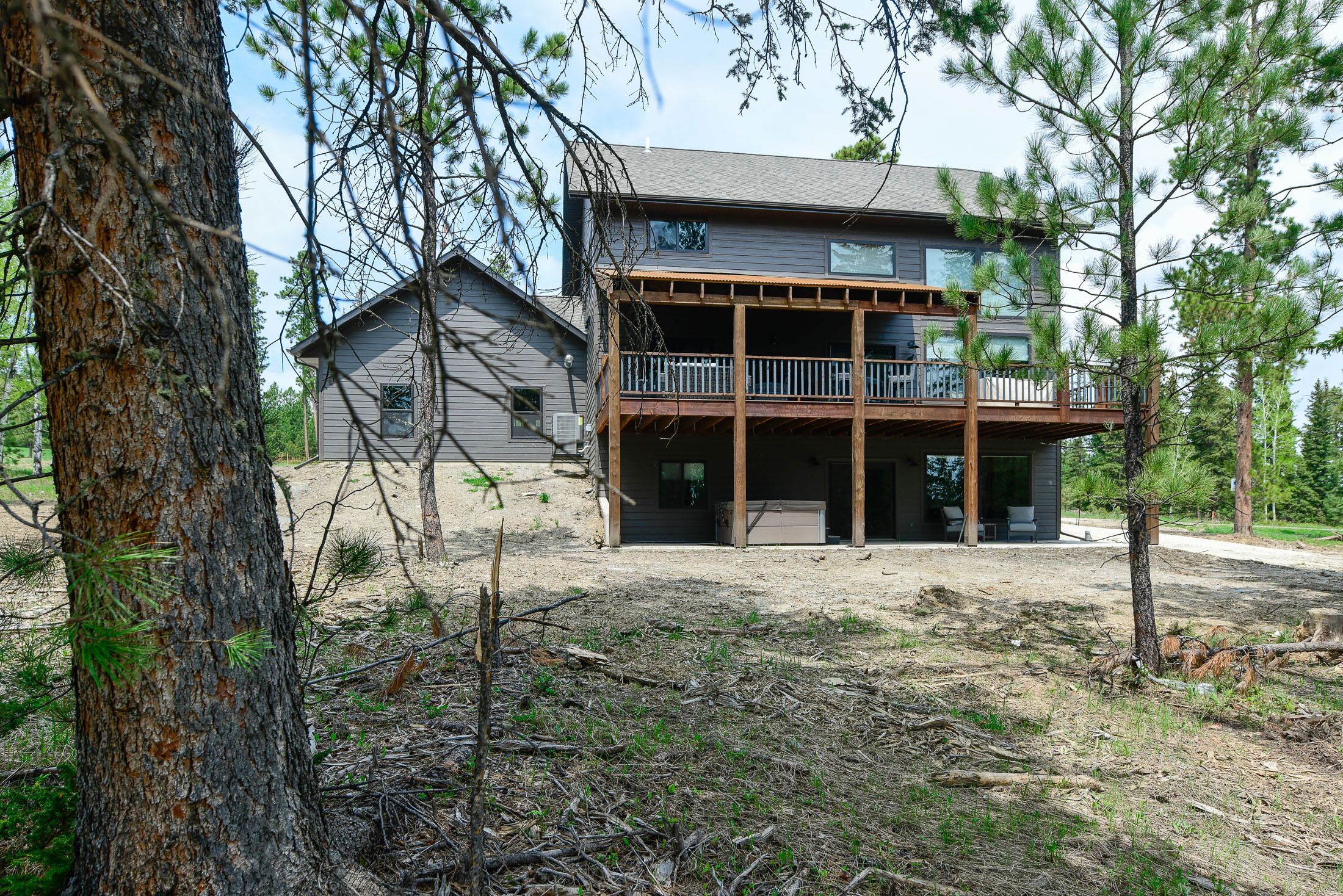 Une maison moderne à deux étages, dotée d’un balcon, entourée d’arbres et bordée d’un terrain sablonneux.