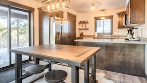 A modern kitchen with a wooden table and stools, stainless steel appliances, and pendant lighting. - Secluded Cabin on 3 Acres w/ Hot Tub, Open Floor Plan, Starlink Internet! (Lead)