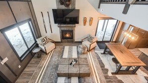 A modern living room with a fireplace, large windows, and a dining area. - Secluded Cabin on 3 Acres w/ Hot Tub, Open Floor Plan, Starlink Internet! (Lead)