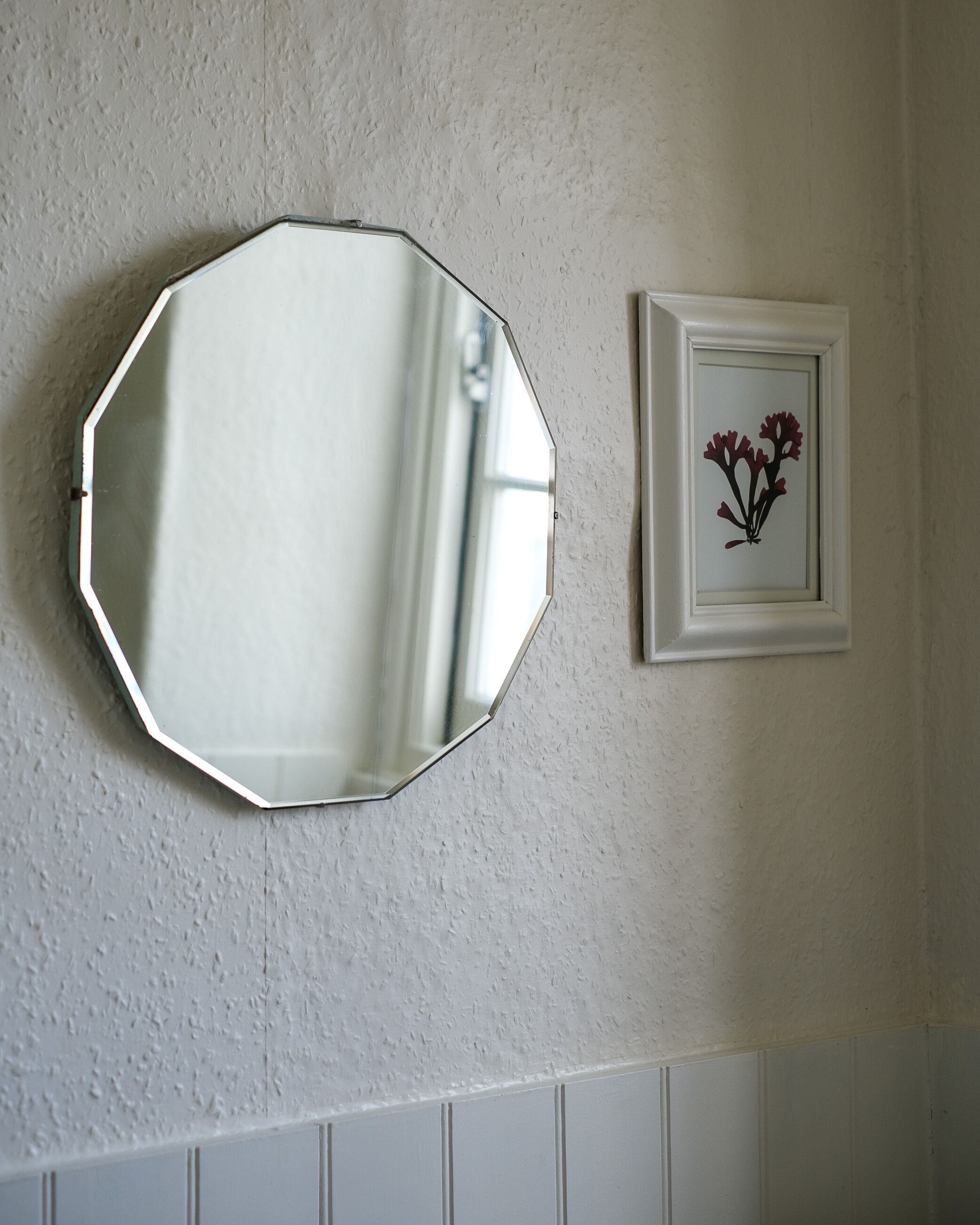 Ein Badezimmer mit einem weißen, achteckigen Spiegel und einem gerahmten Bild von Blumen an der Wand.