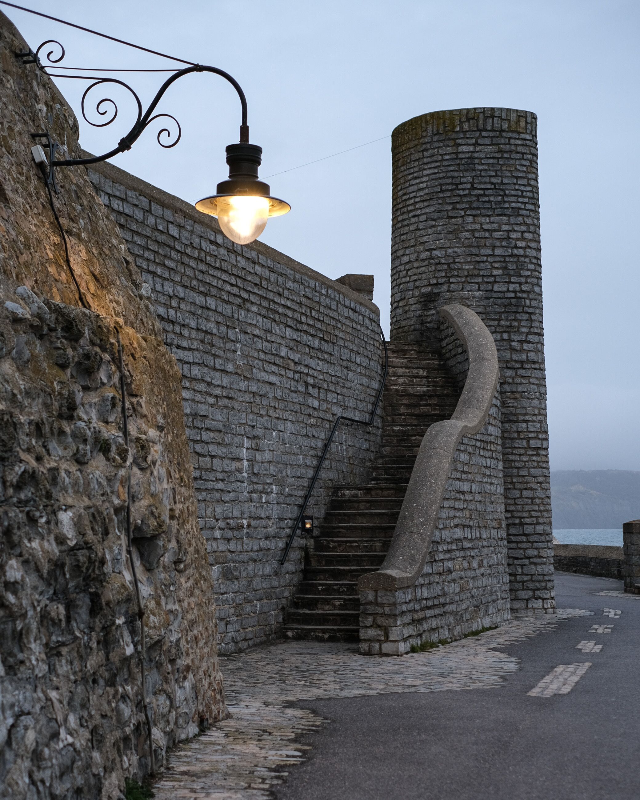 A stone staircase leading up to a turreted building, with a street lamp above.