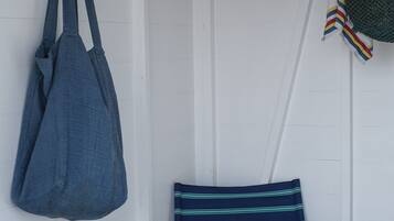 Una silla de madera con un cojín a rayas, una mesita con libros y piedras, y un bolso azul colgado de un gancho.