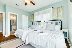 A bedroom with two beds, a ceiling fan, a bathroom with a shower, and a hallway leading to another room. - Sandyland Shores - Screened Porch, Intracoastal & Sea Views! (Surfside Beach)