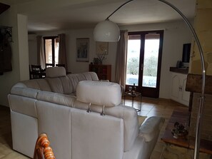 A modern living room with a sectional sofa, a dining area, and a view of the outdoors through large windows.