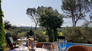 Un área de comedor al aire libre con una mesa preparada para dos personas, rodeada de abundante vegetación y vista a una piscina.