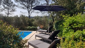 Zona de piscina con sillones reclinables y una sombrilla grande.
