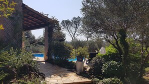 Un camino de piedra que lleva a una zona de piscina rodeada de exuberante vegetación y un pérgola.