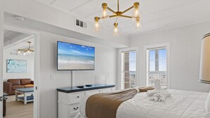 Una camera da letto moderna con un letto grande, una TV a schermo piatto, una scrivania e vista sulla spiaggia dalla finestra.