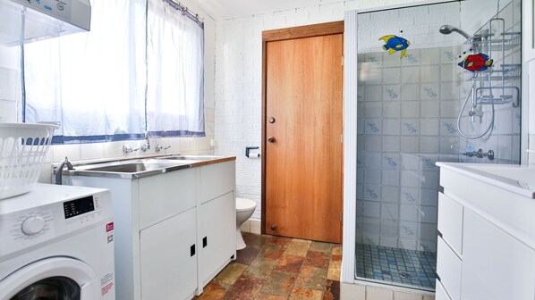 A compact kitchen with a washing machine, a sink, and a shower area with a fish decal.