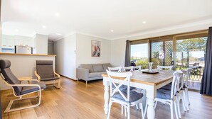 Een moderne woonkamer met een houten eettafel, witte stoelen, een grijze bank en een grijze fauteuil.