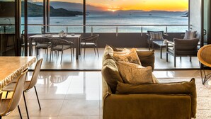 A modern living room with a large sofa, dining table, and chairs, overlooking a scenic sunset view. - Edge Apartment 7, Edge Apartment 7 by HIHA (Hamilton Island)