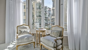 A room with two ornate chairs, a small table, and a view of a cityscape through large windows.