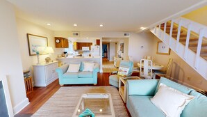 Ein geräumiges Wohnzimmer mit einem hellblauen Sofa, einem Essbereich mit kleinem Tisch und Stühlen sowie einer Küche im Hintergrund.
