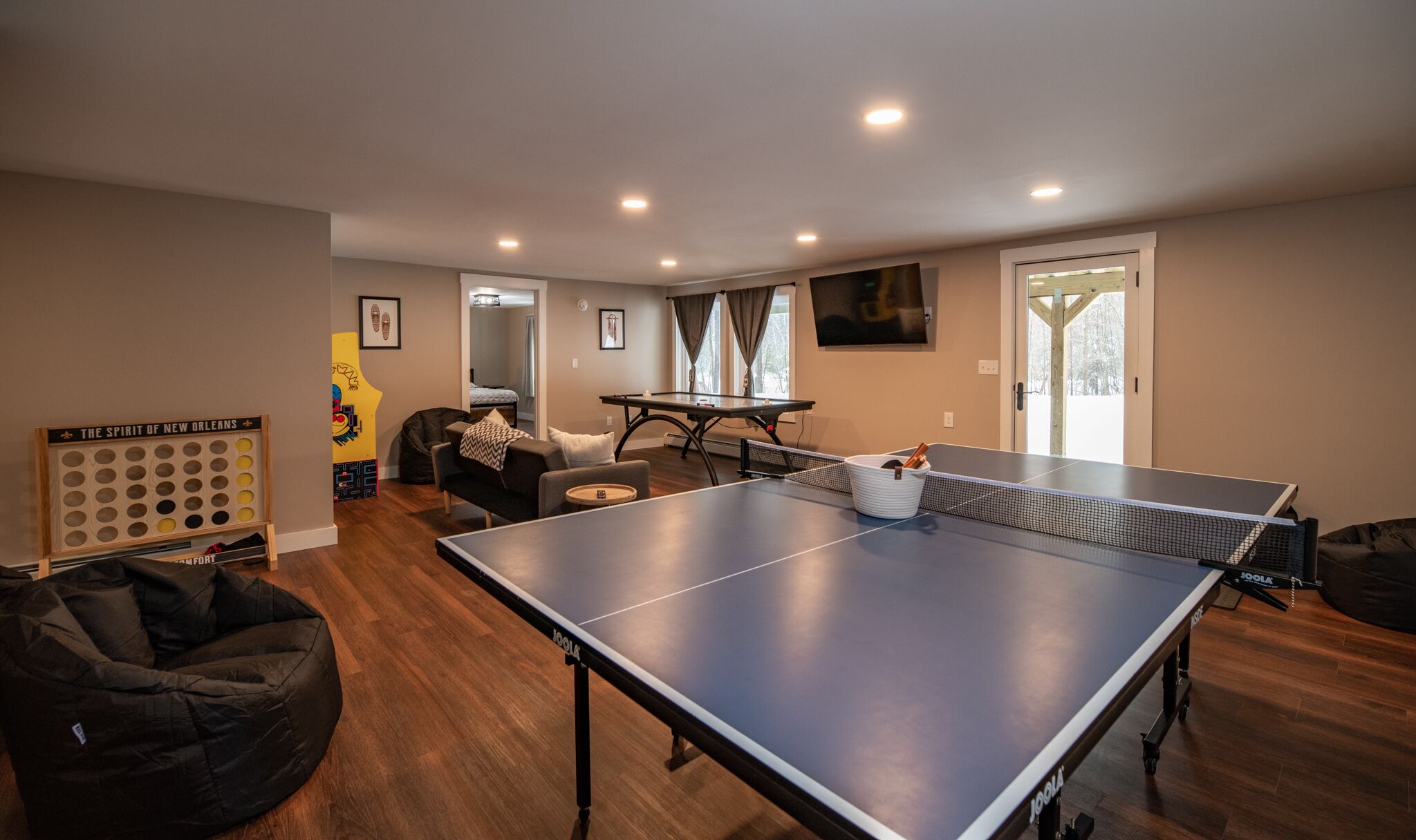 Una habitación amplia con mesa de ping pong, un sillón de peluche y un dardo.