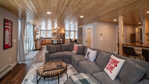 Et moderne interiør med træloft, grå modulsofa og et unikt træsofabord.