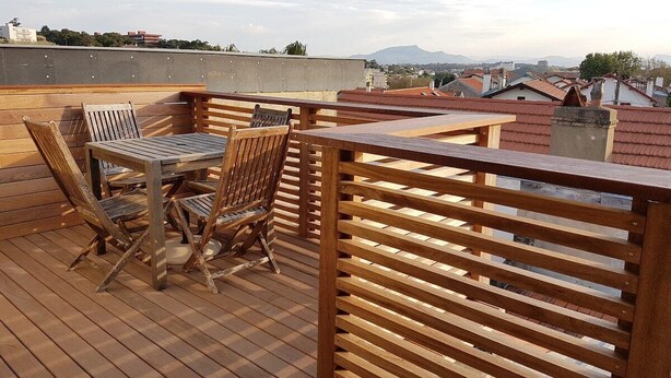 A wooden deck with a table and chairs, overlooking a cityscape with buildings and mountains in the distance. - Biarritz - Beaurivage - Proche côte des Basques (Biarritz)