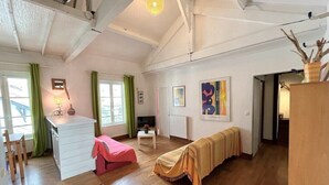 A spacious room with wooden flooring, a white dresser, a pink chair, a bench with a striped blanket, and artwork on the walls. - Biarritz - Beaurivage - Proche côte des Basques (Biarritz)