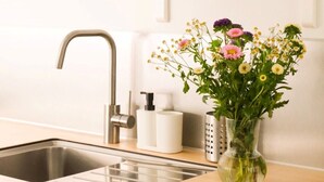 Een keuken met een roestvrijstalen spoelbak, een houten aanrecht en een vaas met bloemen. Boven de spoelbak staan potten op een plank.
