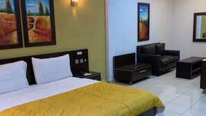 A hotel room with a bed, a sofa, a desk, and two paintings on the wall. - Owee Suites (Lagos)