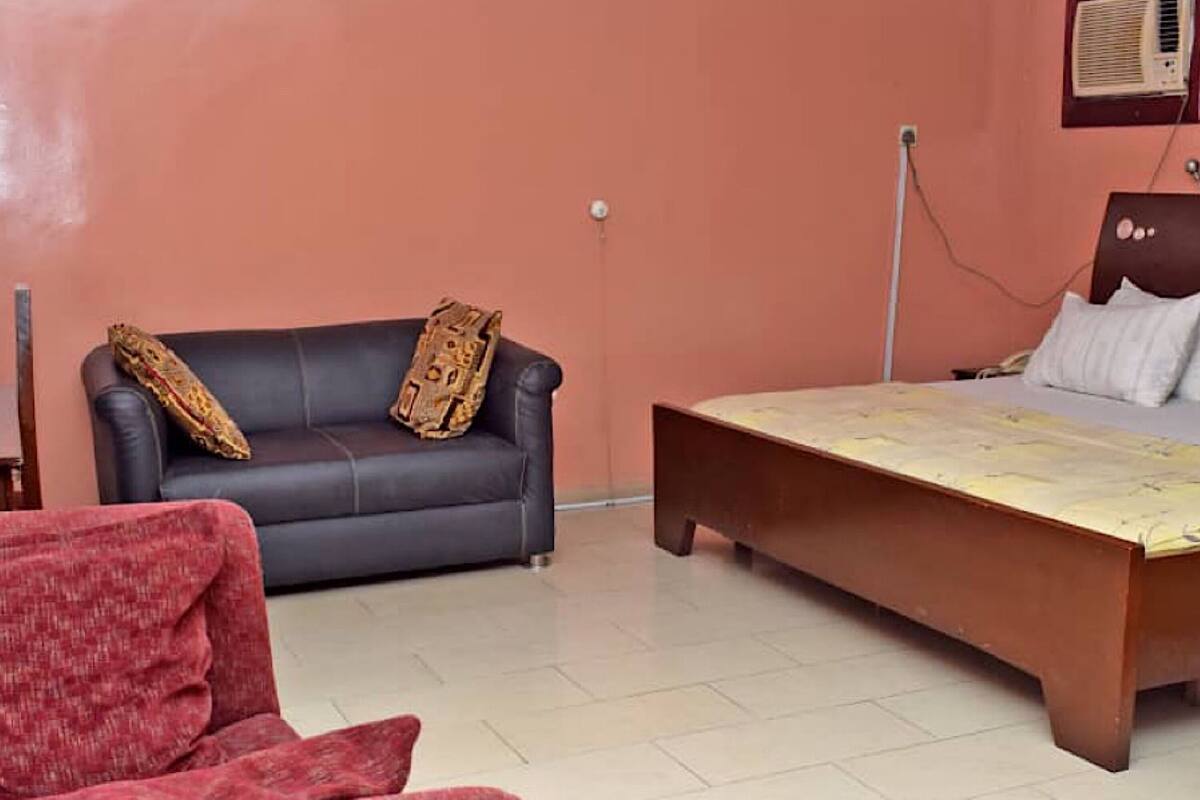 Una habitación con un sofá oscuro, un sillón rojo y una cama de madera con colchón.