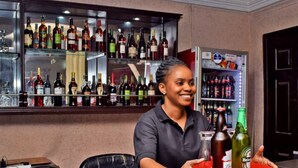 A bar area with a variety of liquor bottles on shelves and a refrigerator stocked with beverages. - Owee Suites (Lagos)