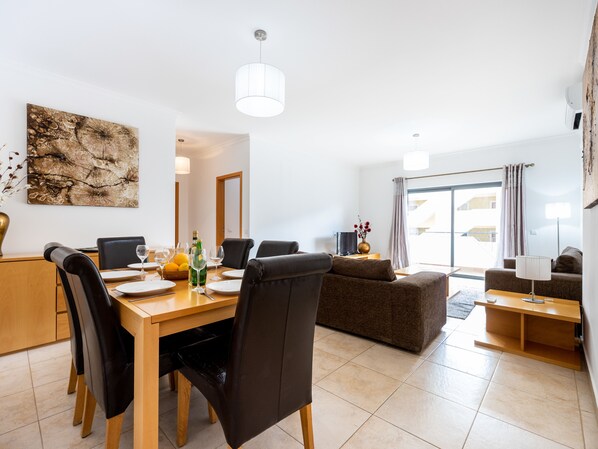 A modern living room with a dining area, a sofa, and a TV. - Quinta das Palmeiras - Apartment Darlene (Lagos)