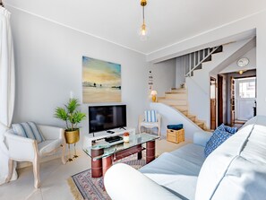 A modern living room with a sofa, TV, and a staircase.