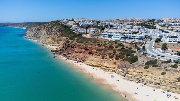 A coastal town with a beach, residential buildings, and a road leading up the hill.