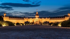 A large, symmetrical building with a central tower, surrounded by well-maintained gardens and a gravel driveway. - Modern apartment Karlsruhe (Karlsruhe)