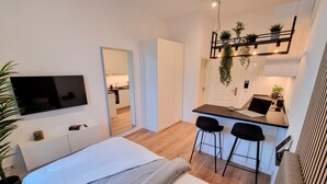 A modern bedroom with a bed, a TV, and a small kitchenette with a bar stool. - Modern apartment Karlsruhe (Karlsruhe)