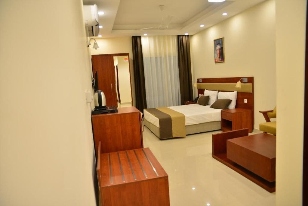 A hotel room with a bed, bedside tables, a desk, and a sofa.
