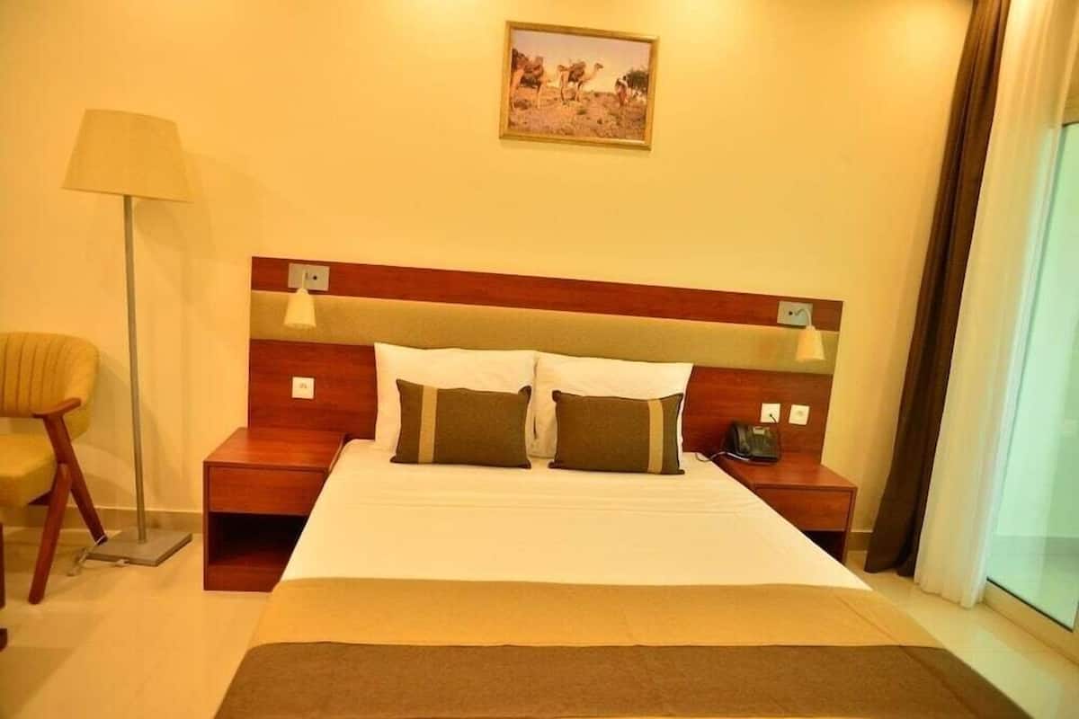 Habitación de hotel con cama, mesitas de noche, lámpara, silla y un cuadro en la pared.
