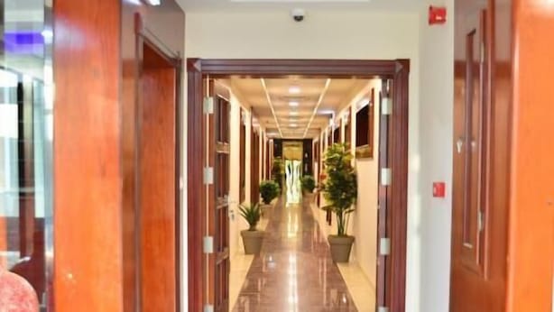 Un pasillo de hotel con puertas de madera, plantas en macetas y suelo de mármol.