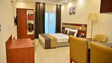 Habitación de hotel con cama, escritorio, silla, lámpara y un cuadro en la pared.
