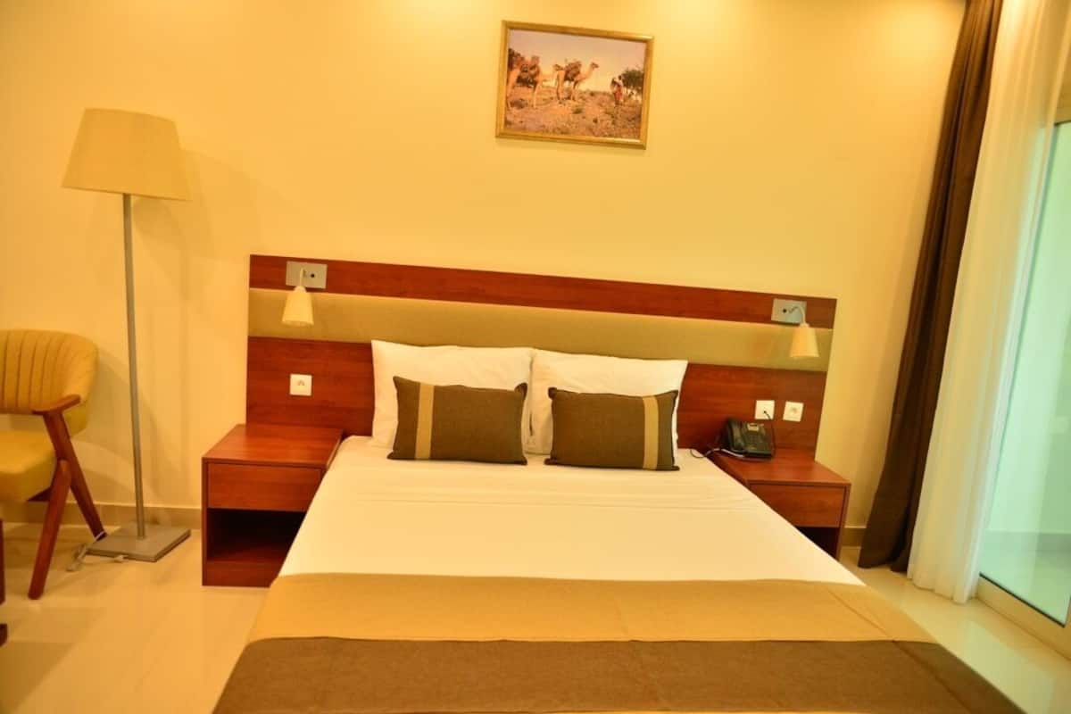 Habitación de hotel con una cama grande, mesitas de noche, una lámpara, una silla y un cuadro en la pared.