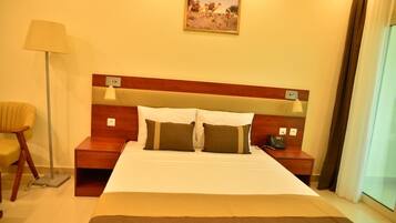 Habitación de hotel con una cama grande, mesitas de noche, una lámpara, una silla y un cuadro en la pared.