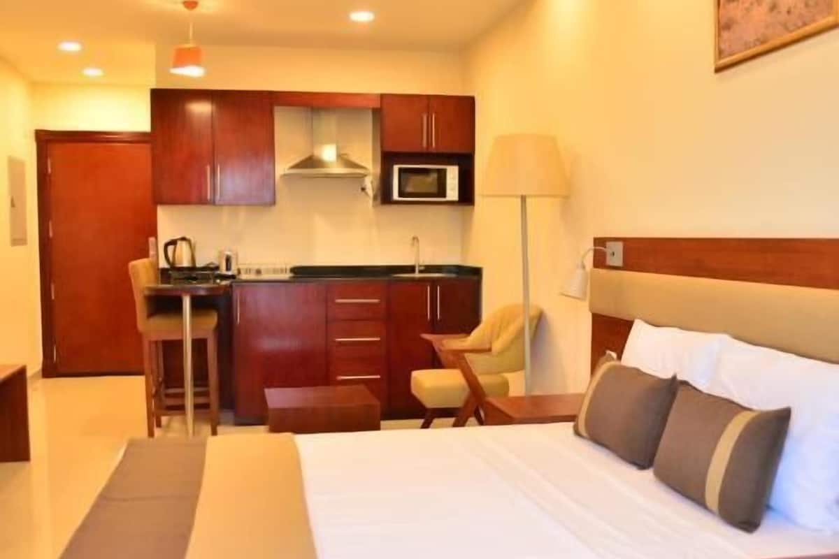 Una habitación de hotel con cama, escritorio, silla, microondas y kitchenette.