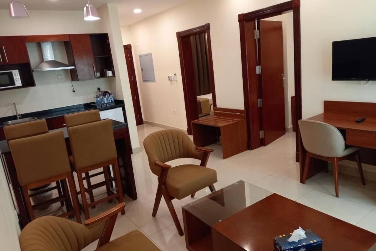 Una habitación de hotel moderna con cocina, un comedor, un sofá, una mesa de centro y un televisor.